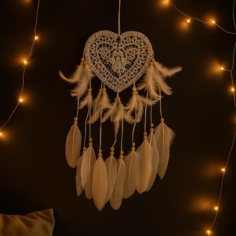 un attrape-rêves en forme de coeur tout en dentelle d'où sont suspendus des plumes blanches et des perles en bois. l'ensemble est poétique, de style bohème et léger.