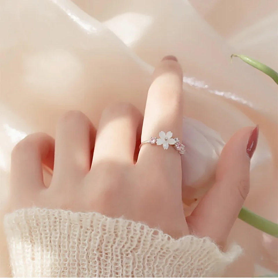 une superbe bague argentée et réglable d'une fleur de sakura blanche accompagnée de petits strass roses et blancs.