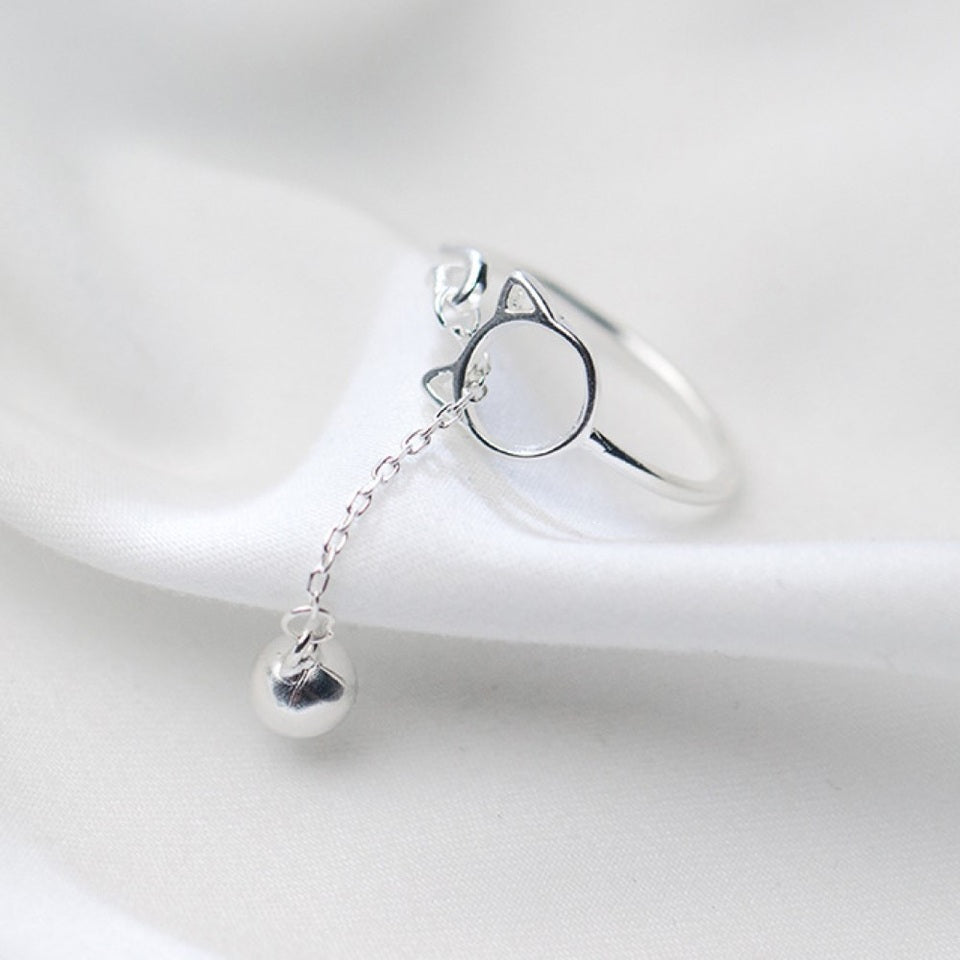 une bague argentée de taille réglable qui forme une tête de chat dans laquelle passe un petit grelot.