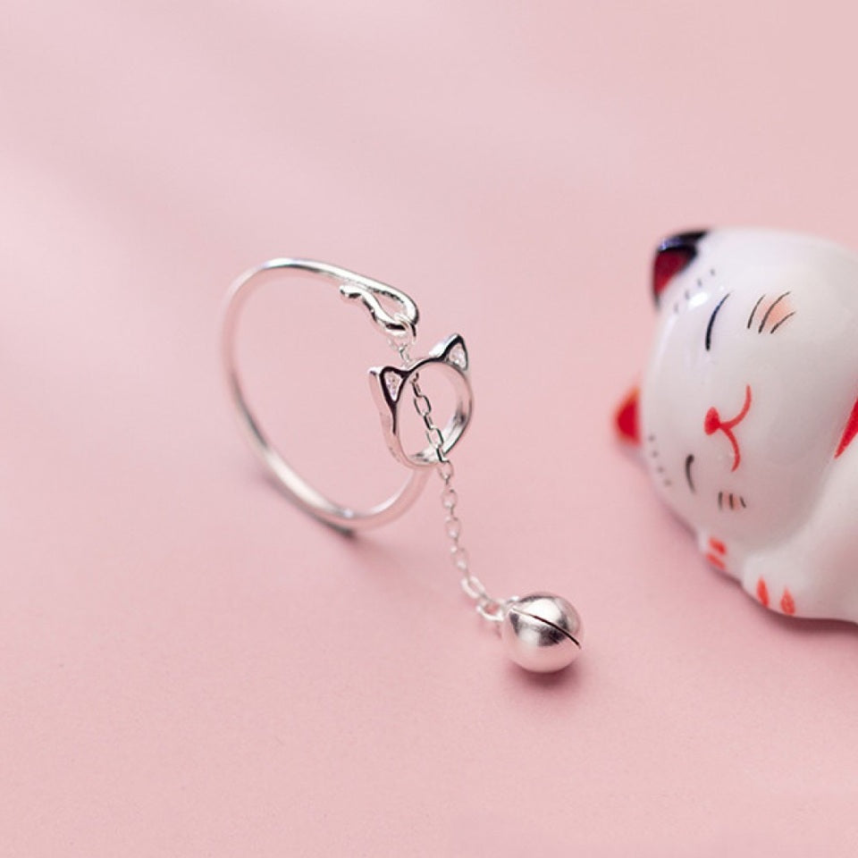 une bague argentée de taille réglable qui forme une tête de chat dans laquelle passe un petit grelot.