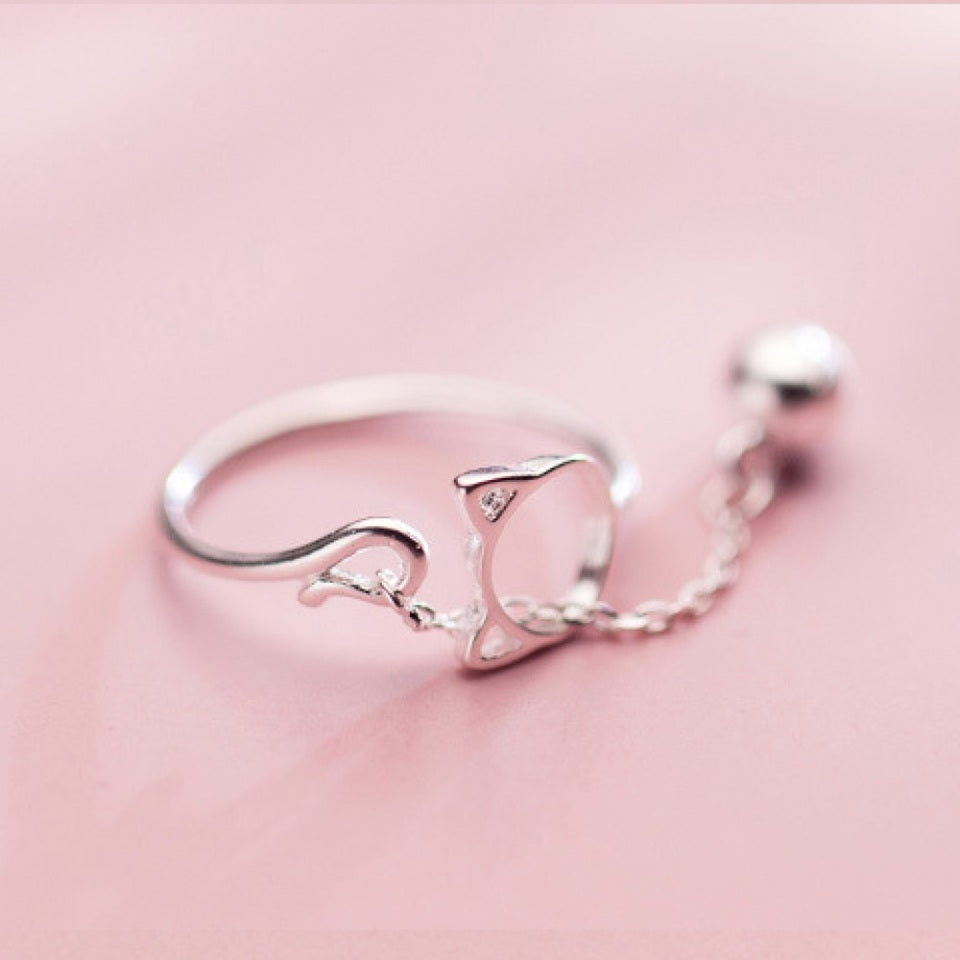 une bague argentée de taille réglable qui forme une tête de chat dans laquelle passe un petit grelot.