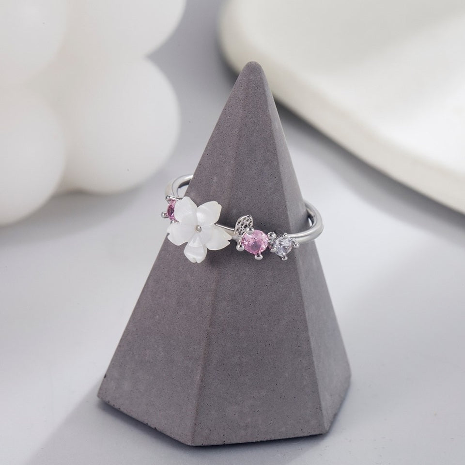 une superbe bague argentée et réglable d'une fleur de sakura blanche accompagnée de petits strass roses et blancs.