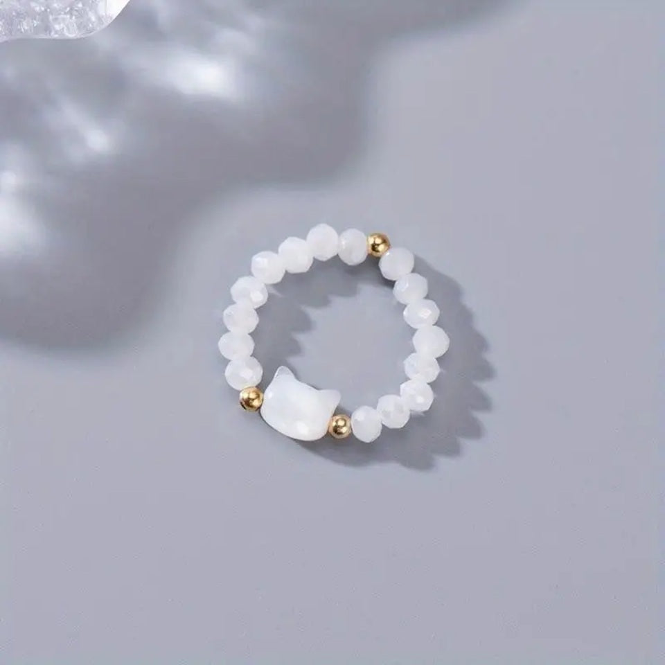 une bague taille élastique toute en parles et une breloque perles en forme de tête de chat. Disponible en coloris noir ou blanc.