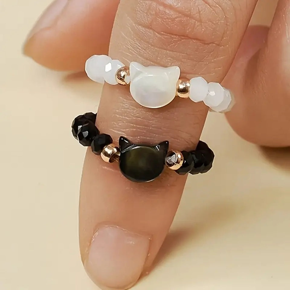 une bague taille élastique toute en parles et une breloque perles en forme de tête de chat. Disponible en coloris noir ou blanc.