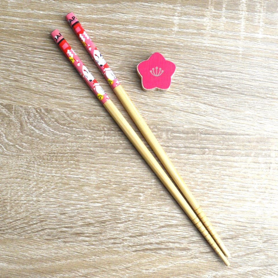 une paire de baguettes japonaises en bambou décoré d'un mignon kitsune et son repose baguette en forme de fleur de sakura rouge. Elégance et folklore japonais réunis pour une table élégante.