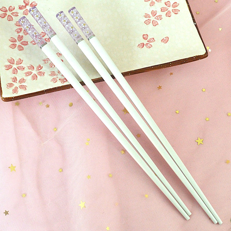 une paire de baguettes japonaises blanches dont le bout est transparent et violet et est décoré de jolies fleurs de sakura blanches