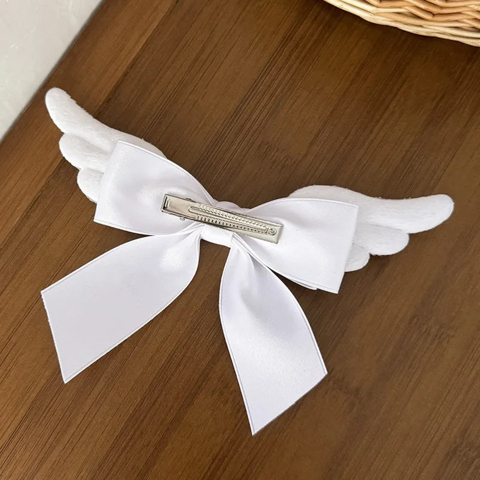 Barrette à cheveux blanche en forme de nœud avec ailes d'ange, présentée sur une table en chêne. Cet accessoire romantique et élégant apporte une touche poétique à toutes les coiffures et constitue une jolie idée cadeau pour les amateurs d'accessoires mignons.