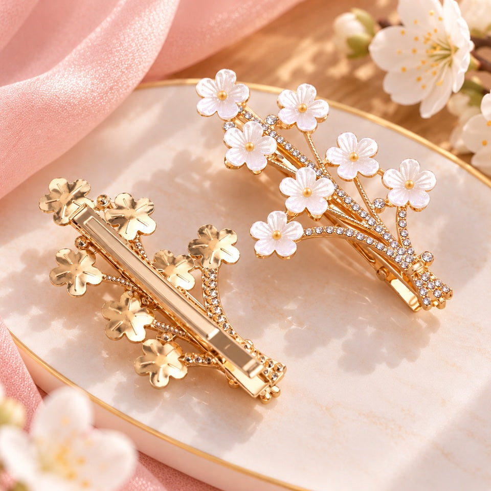 Deux vues d’une barrette à cheveux dorée en forme de branche de prunier, ornée de fleurs blanches nacrées et de strass brillants.