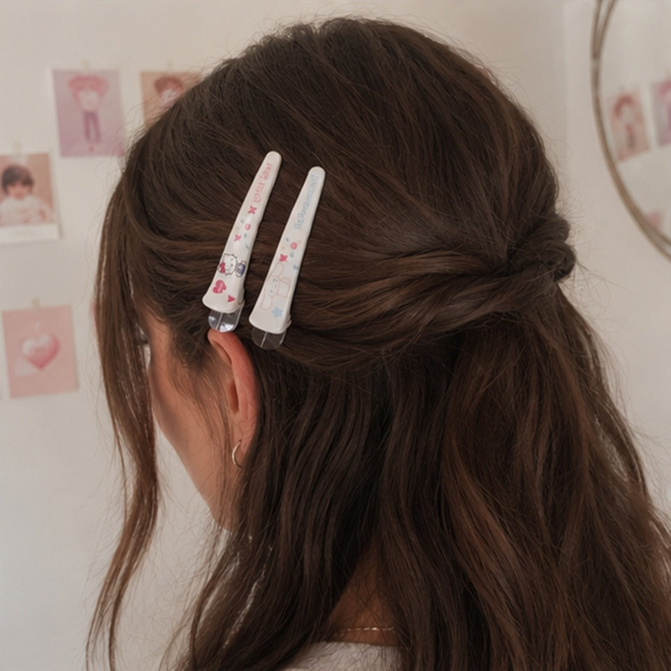 Vue arrière d'une coiffure semi-attachée mettant en valeur deux barrettes à cheveux blanches illustrées de personnages kawaii. Les accessoires sont portés par une femme de type occidental dans un intérieur aux tons pastel.