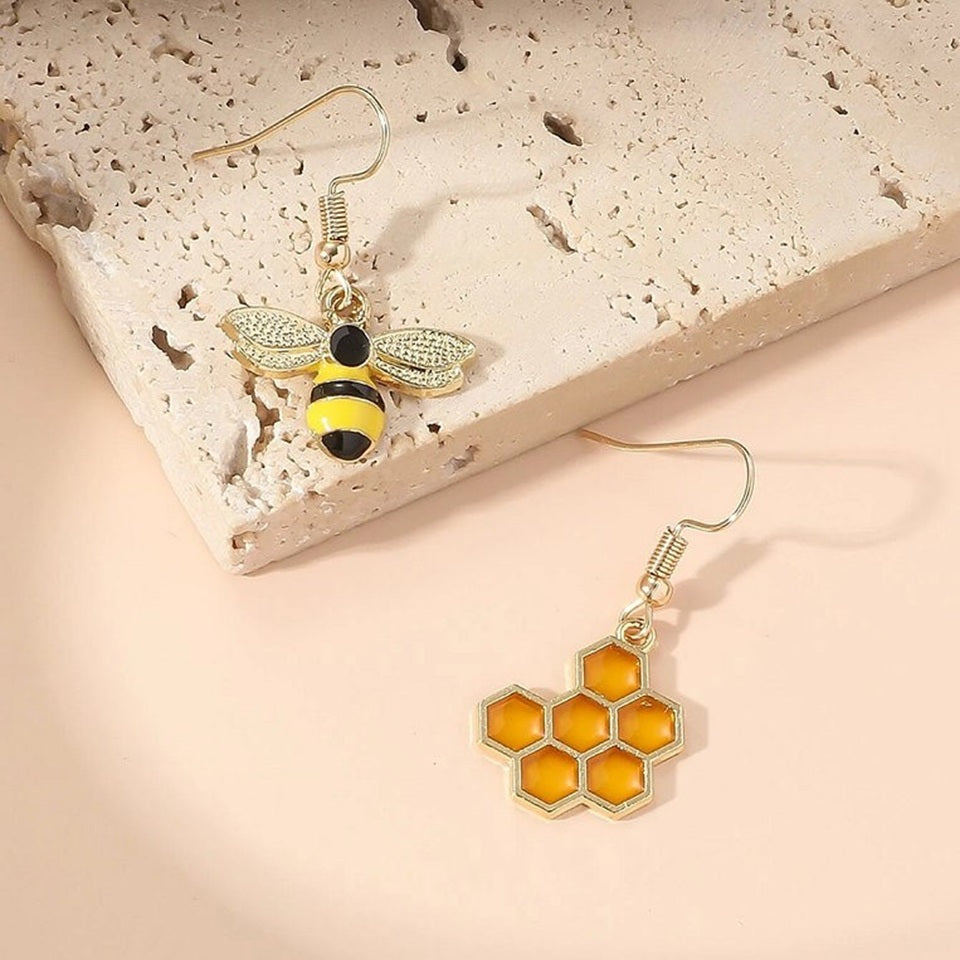 une paire de boucles d'oreilles asymétriques, d'un côté une abeille en strass et de l'autre un rayon de miel