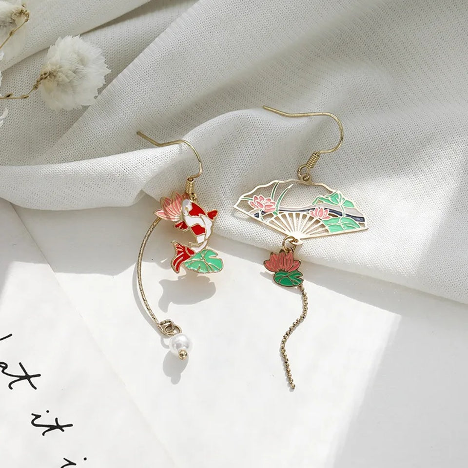 une paire de boucles d'oreilles asymétriques composées d'une carpe koï rouge et blanche et d'une perle ainsi que d'un éventail au motif de nénuphar.