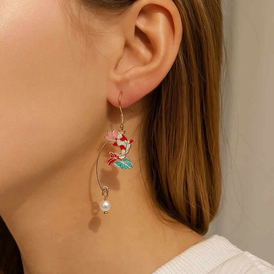 une paire de boucles d'oreilles asymétriques composées d'une carpe koï rouge et blanche et d'une perle ainsi que d'un éventail au motif de nénuphar.