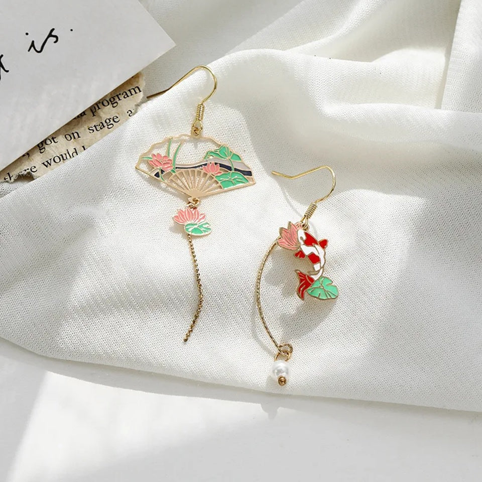 une paire de boucles d'oreilles asymétriques composées d'une carpe koï rouge et blanche et d'une perle ainsi que d'un éventail au motif de nénuphar.