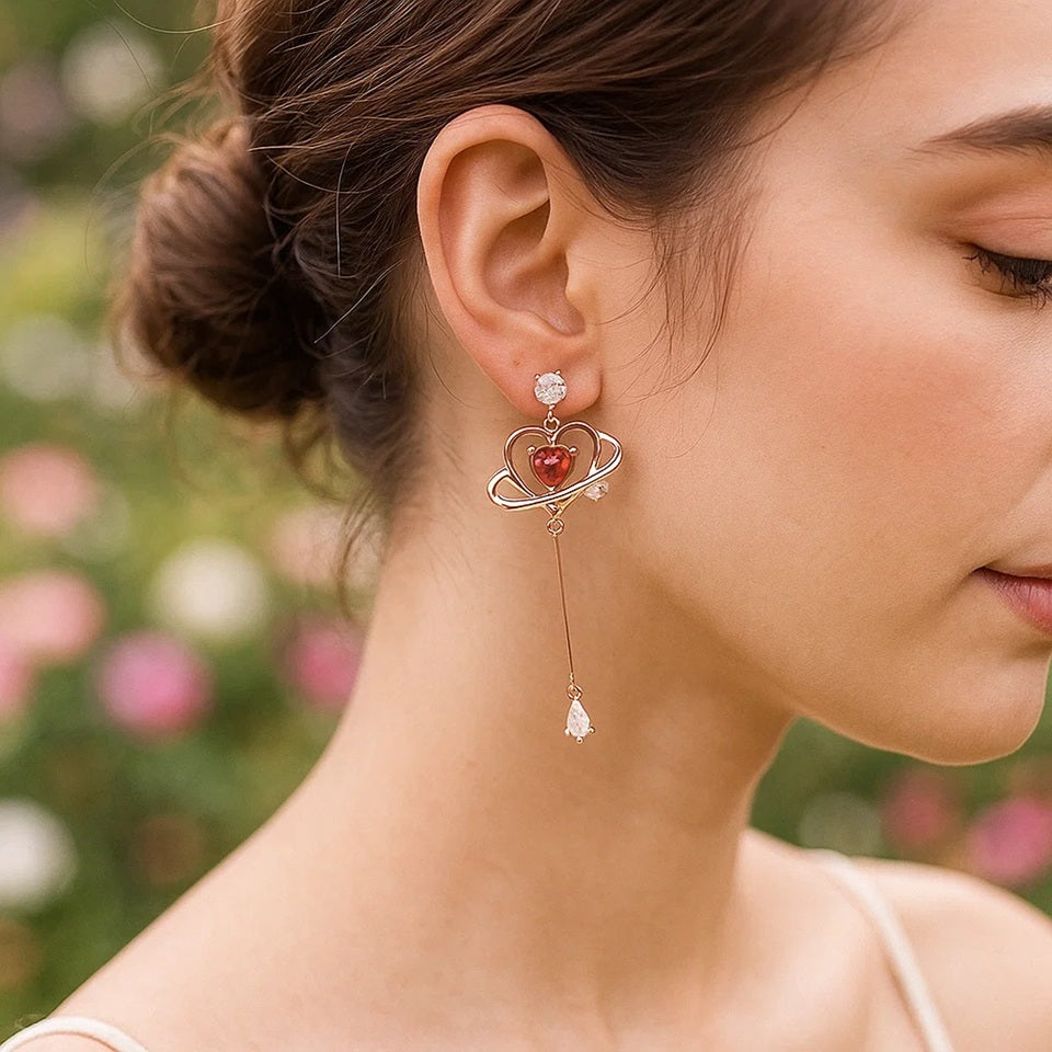 des boucles d'oreilles au design romantique et féminin : une structure en forme de coeur doré abrite une strass rose en forme de coeur, tel le coeur d'une planète. Au bout, est suspendu un strass brillant en forme de goutte.
