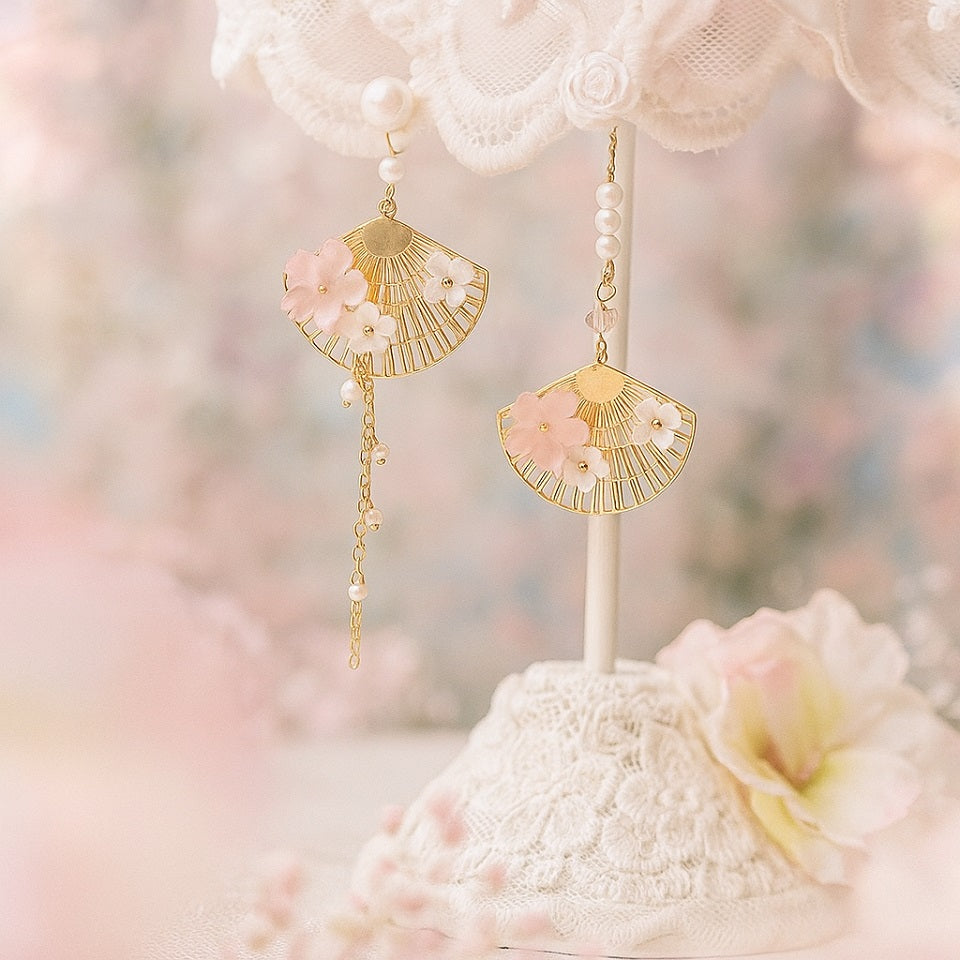 une paire de boucles d'oreilles asymétriques composées d'éventails dorés décorés avec de jolies fleurs de sakura, des perles blanches viennent apporter de l'élégance à l'ensemble.