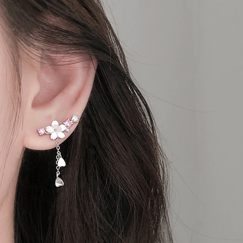 une paire de boucles d'oreilles qui épousent le lobe de l'oreille avec délicatesse et élégance. Une jolie fleur de sakura blanche et des strass blancs et roses viennent embellir l'ensemble. ne petite chaine pendante ornée de pétale de sakura est suspendue aux boucles.