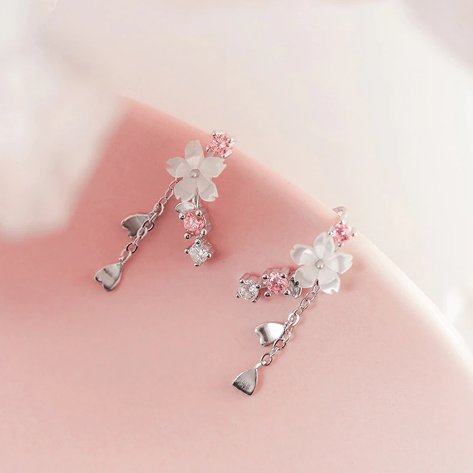 une paire de boucles d'oreilles qui épousent le lobe de l'oreille avec délicatesse et élégance. Une jolie fleur de sakura blanche et des strass blancs et roses viennent embellir l'ensemble. ne petite chaine pendante ornée de pétale de sakura est suspendue aux boucles.