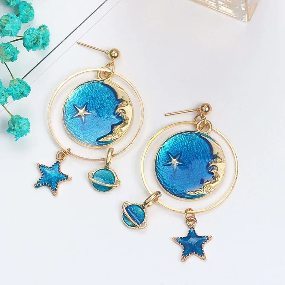 des boucles d'oreilles en forme de planète où se croisent lune dorée et étoiles. Les couleurs bleue et doré se marient parfaitement entre elles.