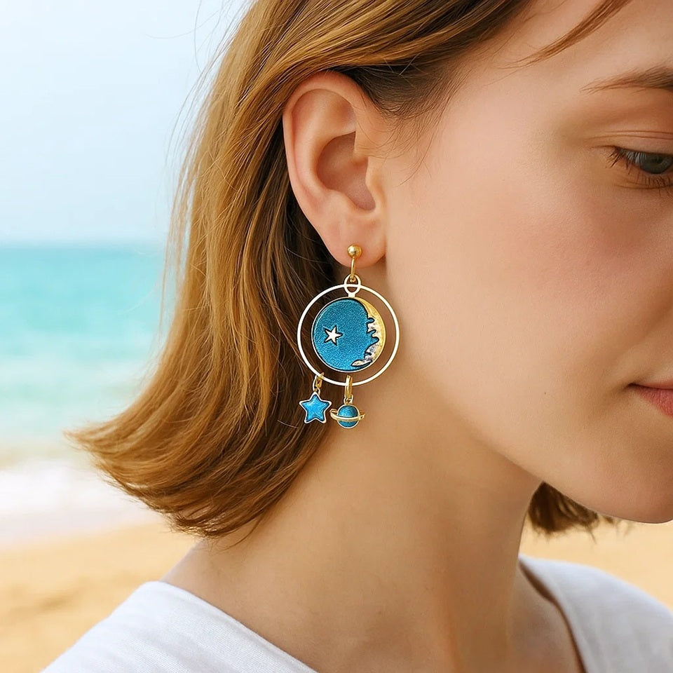des boucles d'oreilles en forme de planète où se croisent lune dorée et étoiles. Les couleurs bleue et doré se marient parfaitement entre elles.