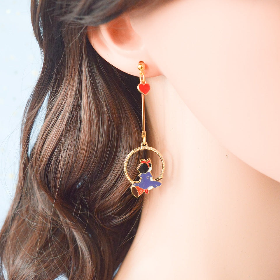 une paire de boucles d'oreilles asymétriques inspirées de Kiki la petite sorcière. D'un côté il y a Jiji le chat noir et de l'autre, Kiki sur son balai.