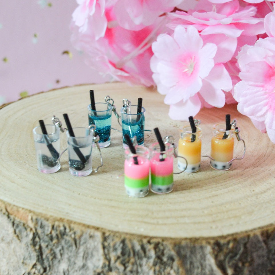 des boucles d'oreilles en forme de bubble tea de couleurs différentes. Certaines sont pailletées. Elles ont une paille pour plus de réalisme.