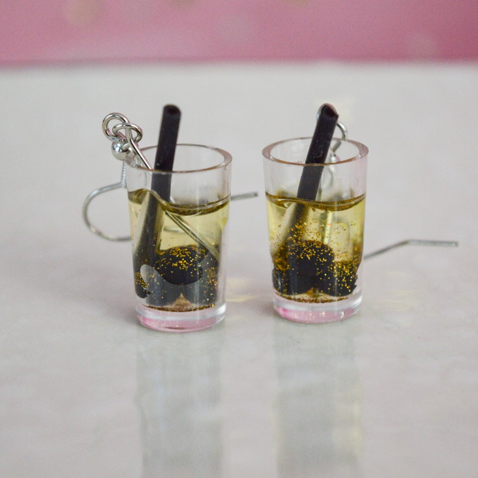 des boucles d'oreilles en forme de bubble tea de couleurs différentes. Certaines sont pailletées. Elles ont une paille pour plus de réalisme.