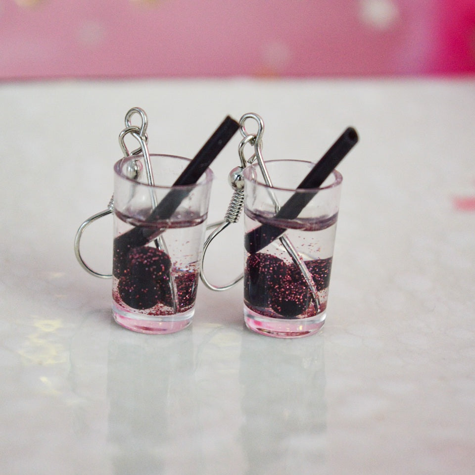 des boucles d'oreilles en forme de bubble tea de couleurs différentes. Certaines sont pailletées. Elles ont une paille pour plus de réalisme.
