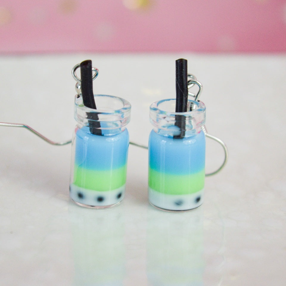 des boucles d'oreilles en forme de bubble tea de couleurs différentes. Certaines sont pailletées. Elles ont une paille pour plus de réalisme.
