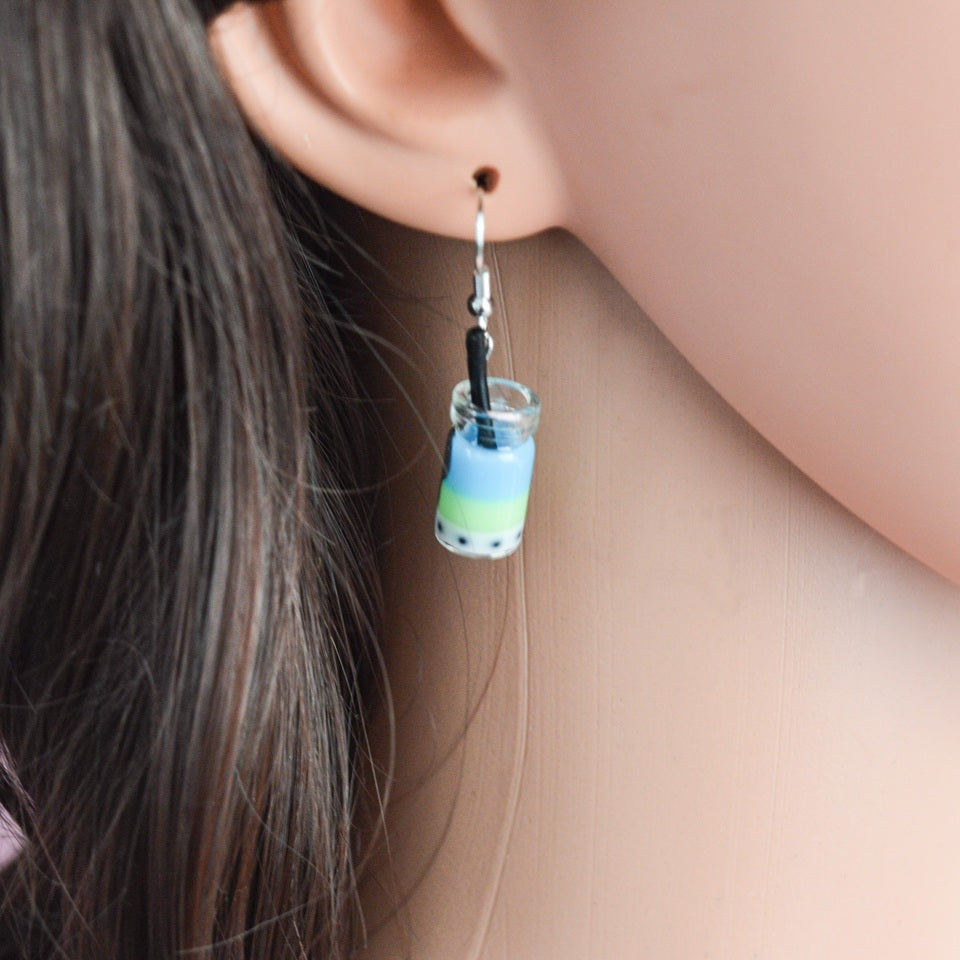 des boucles d'oreilles en forme de bubble tea de couleurs différentes. Certaines sont pailletées. Elles ont une paille pour plus de réalisme.