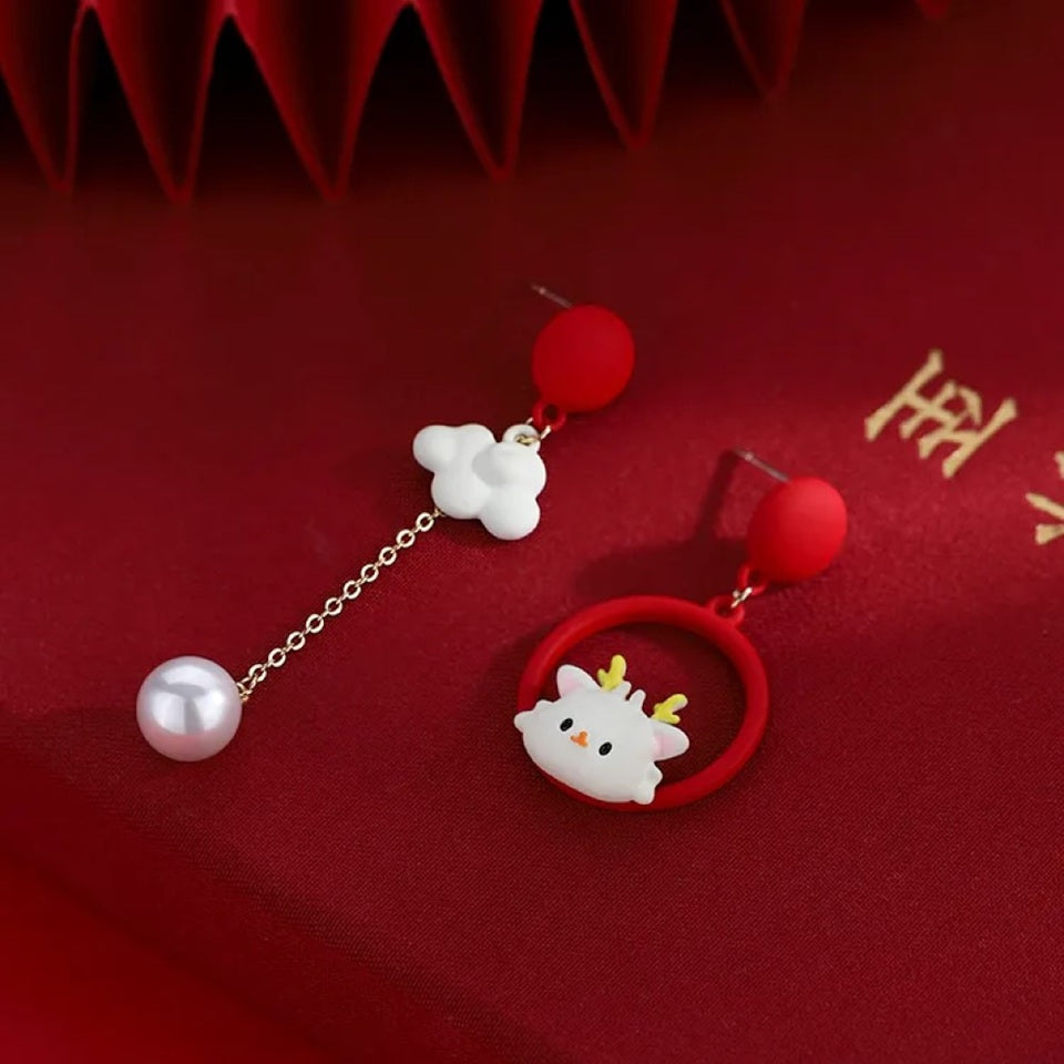 une paire de boucles d'oreilles asymétriques : d'un côté un cerf au design totalement kawaii, de l'autre un adorable nuage blanc et sa perle. L'ensemble est de couleur blanc et rouge.