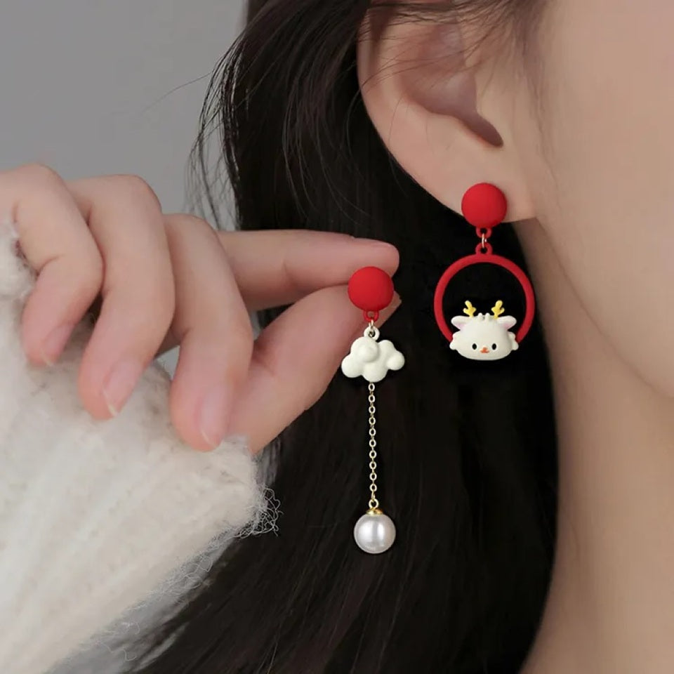 une paire de boucles d'oreilles asymétriques : d'un côté un cerf au design totalement kawaii, de l'autre un adorable nuage blanc et sa perle. L'ensemble est de couleur blanc et rouge.