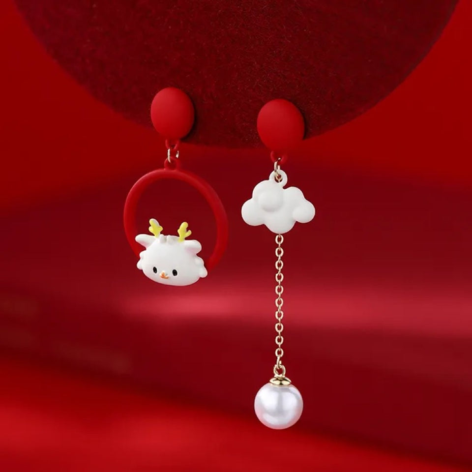 une paire de boucles d'oreilles asymétriques : d'un côté un cerf au design totalement kawaii, de l'autre un adorable nuage blanc et sa perle. L'ensemble est de couleur blanc et rouge.