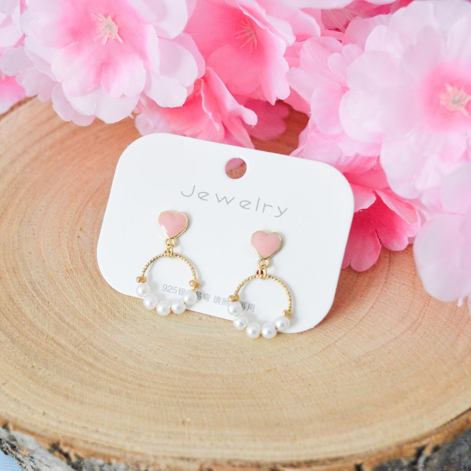 des boucles d'oreilles composées d'un coeur rose et d'une ronde de perles blanches pour un style romantique