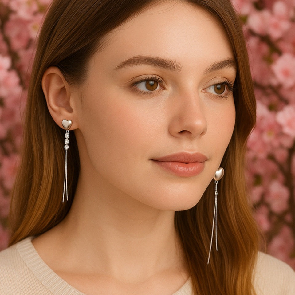 des boucles d'oreilles asymétriques et argentées en forme de cœurs. De jolis strass brillants viennent s'y ajouter ainsi que des chainettes.