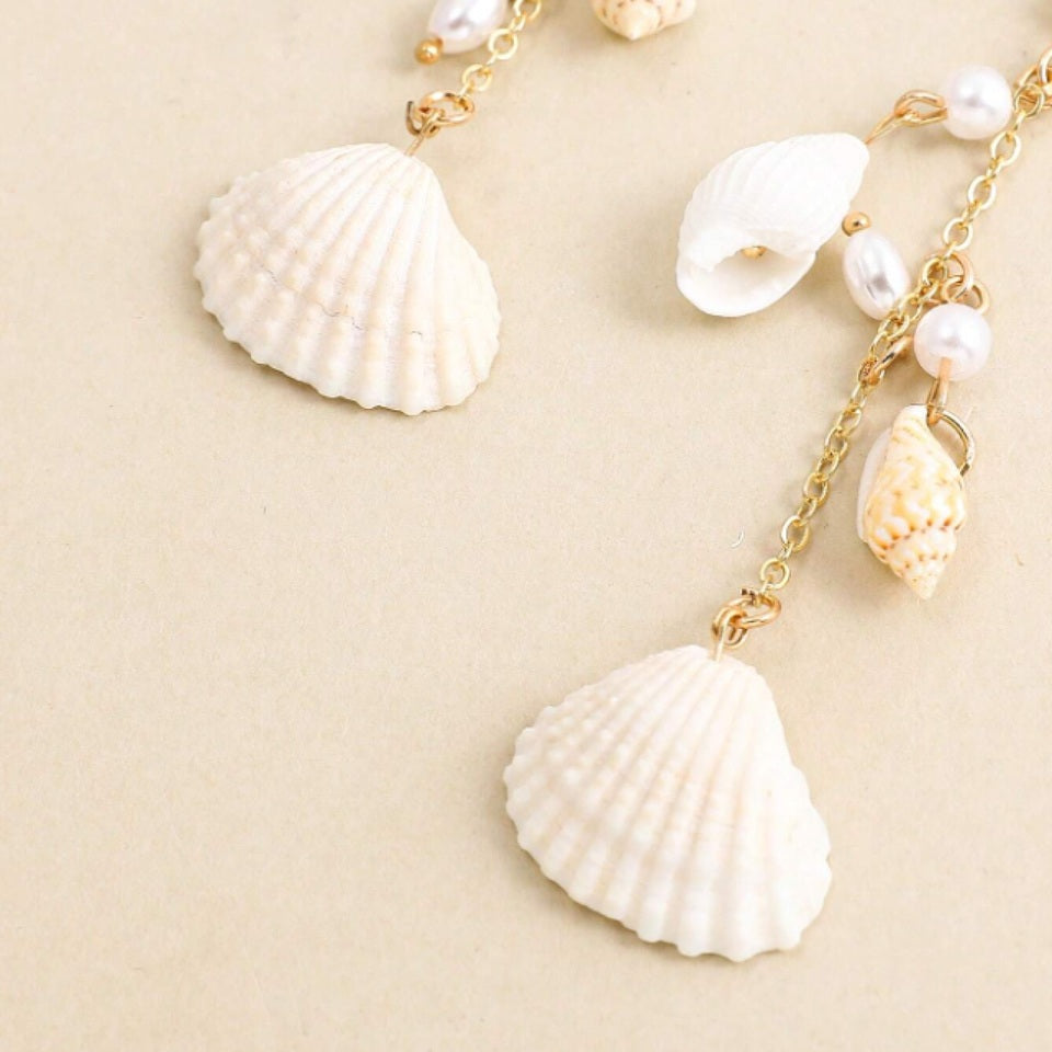 des boucles d'oreilles longues et dorées formées de divers coquillages blancs. L'ensemble évoque les vacances, la plage et l'été.
