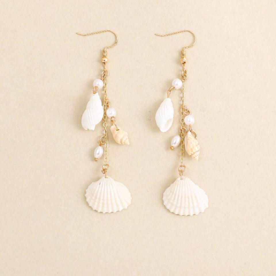 des boucles d'oreilles longues et dorées formées de divers coquillages blancs. L'ensemble évoque les vacances, la plage et l'été.