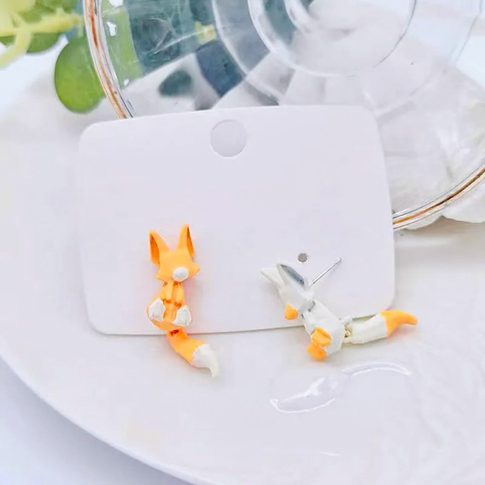 des boucles d'oreilles composées de deux renards : un blanc et un roux. Leur queue est pendante et le design est très mignon