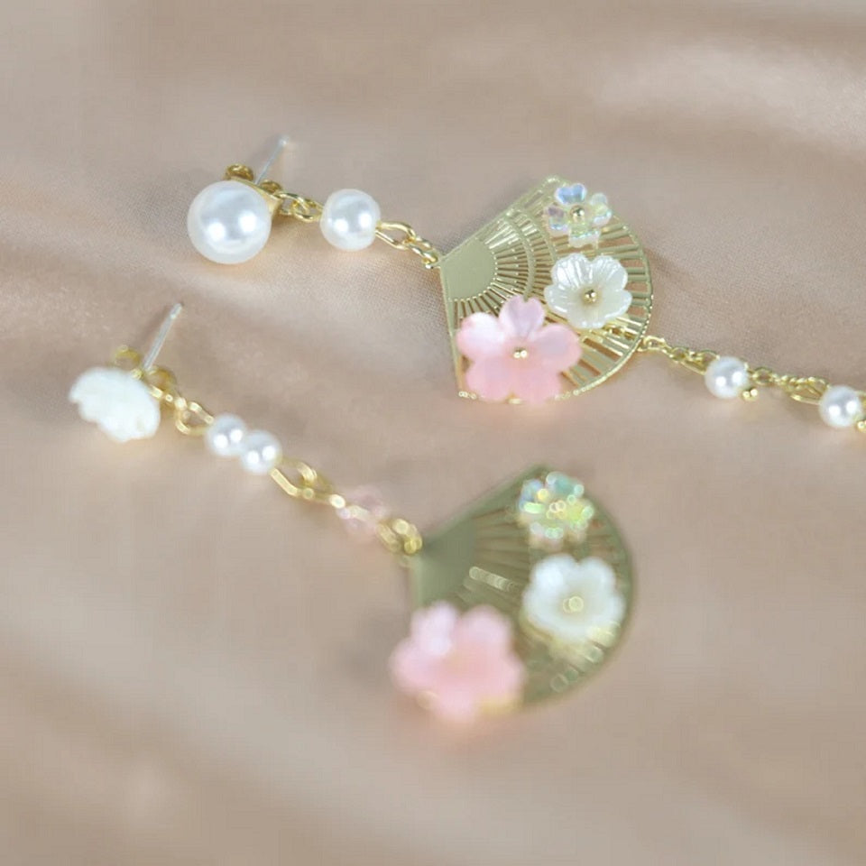 une paire de boucles d'oreilles asymétriques composées d'éventails dorés décorés avec de jolies fleurs de sakura, des perles blanches viennent apporter de l'élégance à l'ensemble.