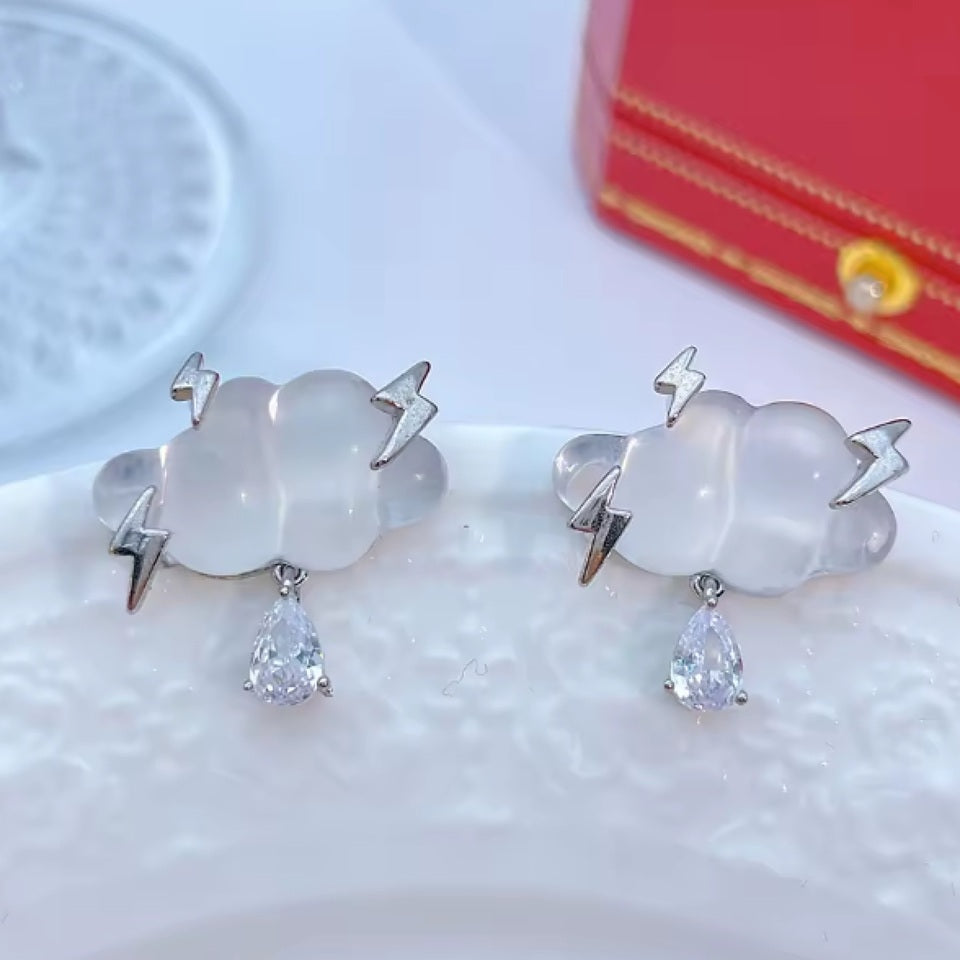 une paire de boucles d'oreilles en forme de nuage transparents d'où pendent un joli strass en forme de goutte. Des éclairs habillent les nuages