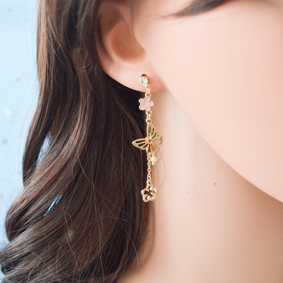 une paire de boucles d'oreilles asymétriques composées d'un papillon doré et de fleurs de sakura rose