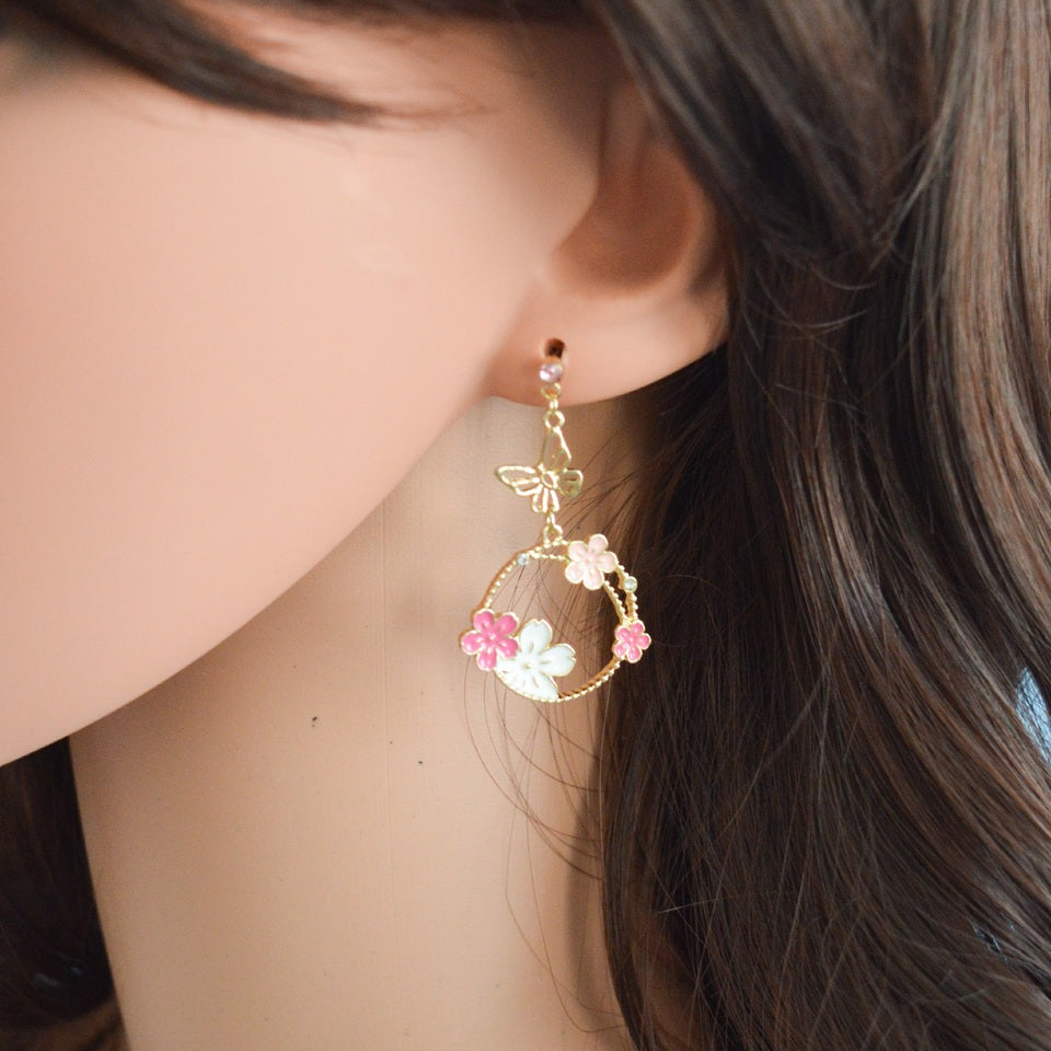 une paire de boucles d'oreilles asymétriques composées d'un papillon doré et de fleurs de sakura rose