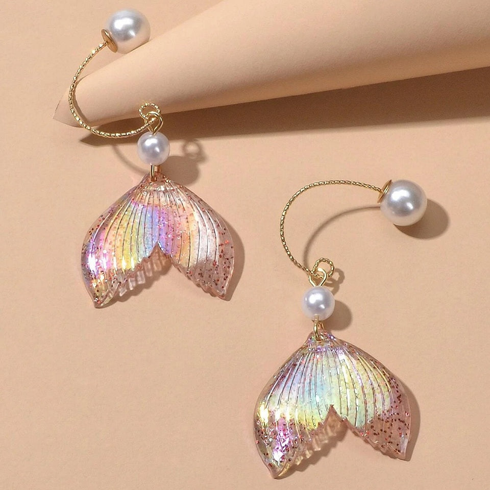 des boucles d'oreilles en forme de queues de sirènes pailletées et roses. De jolies perles blanches viennent ajouter de l'élégance à l'ensemble