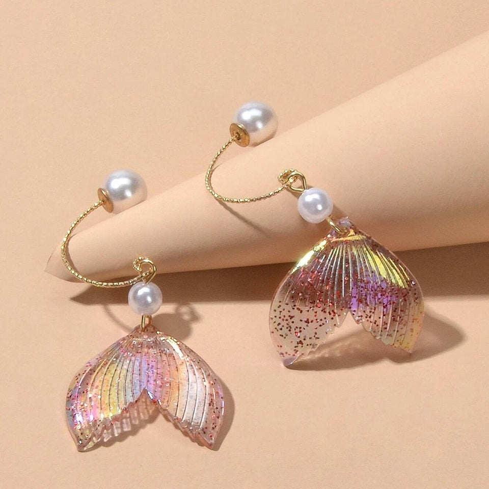 des boucles d'oreilles en forme de queues de sirènes pailletées et roses. De jolies perles blanches viennent ajouter de l'élégance à l'ensemble