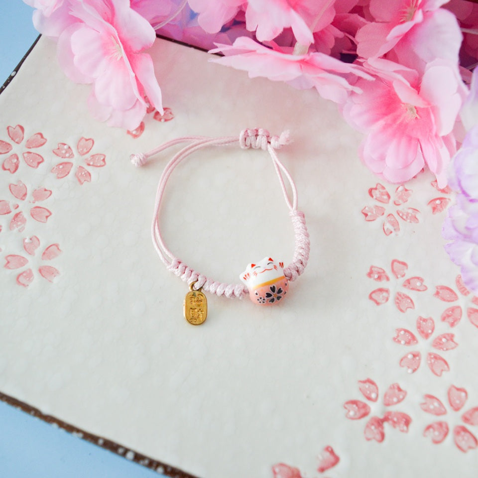 un bracelet en tissu en forme d'un maneki neko coloré avec sa plaquette dorée. Symbole de chance, de bonne fortune, il est inspiré du style japonais
