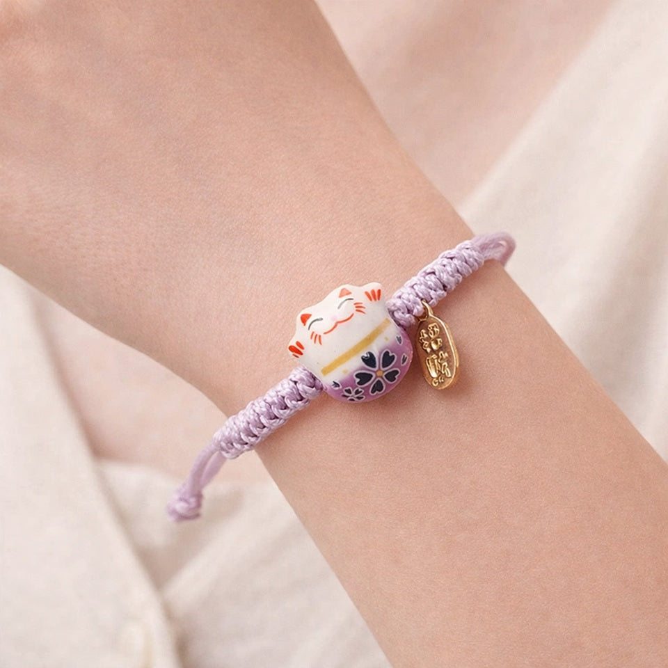 un bracelet en tissu en forme d'un maneki neko coloré. Symbole de chance, de bonne fortune, il est inspiré du style japonais