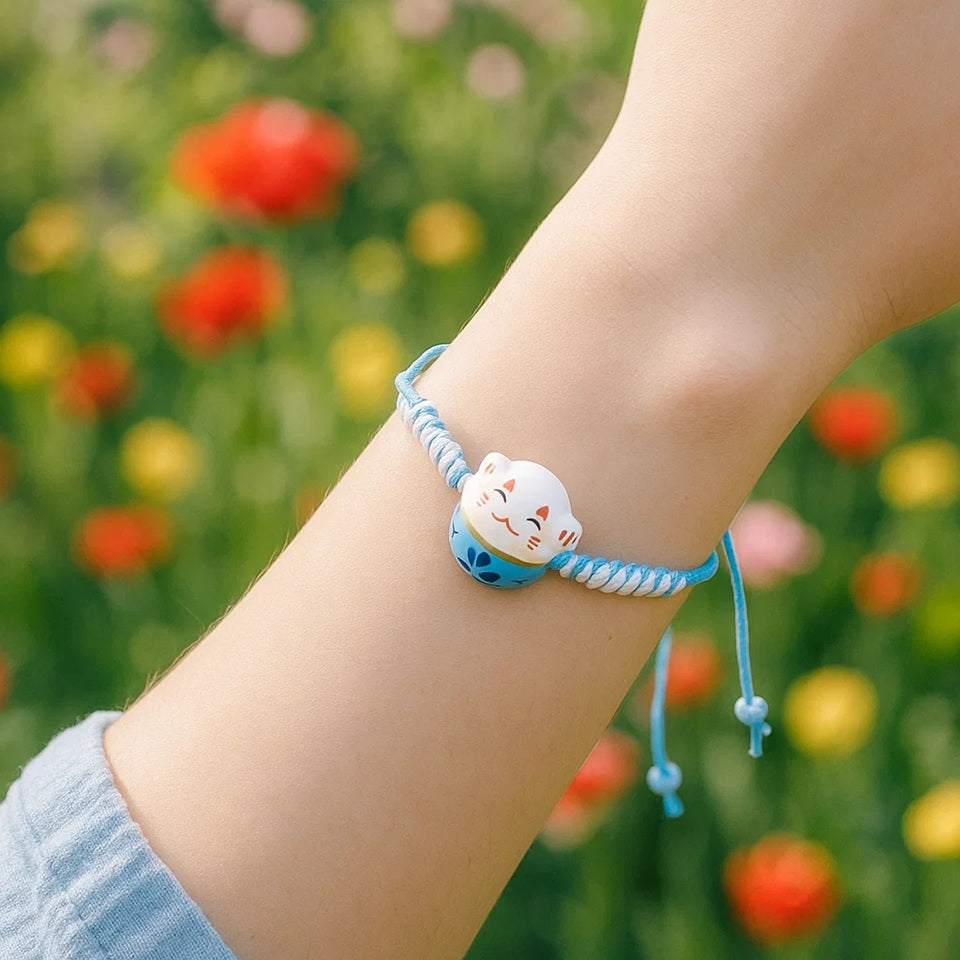 un bracelet en tissu en forme d'un maneki neko coloré. Symbole de chance, de bonne fortune, il est inspiré du style japonais