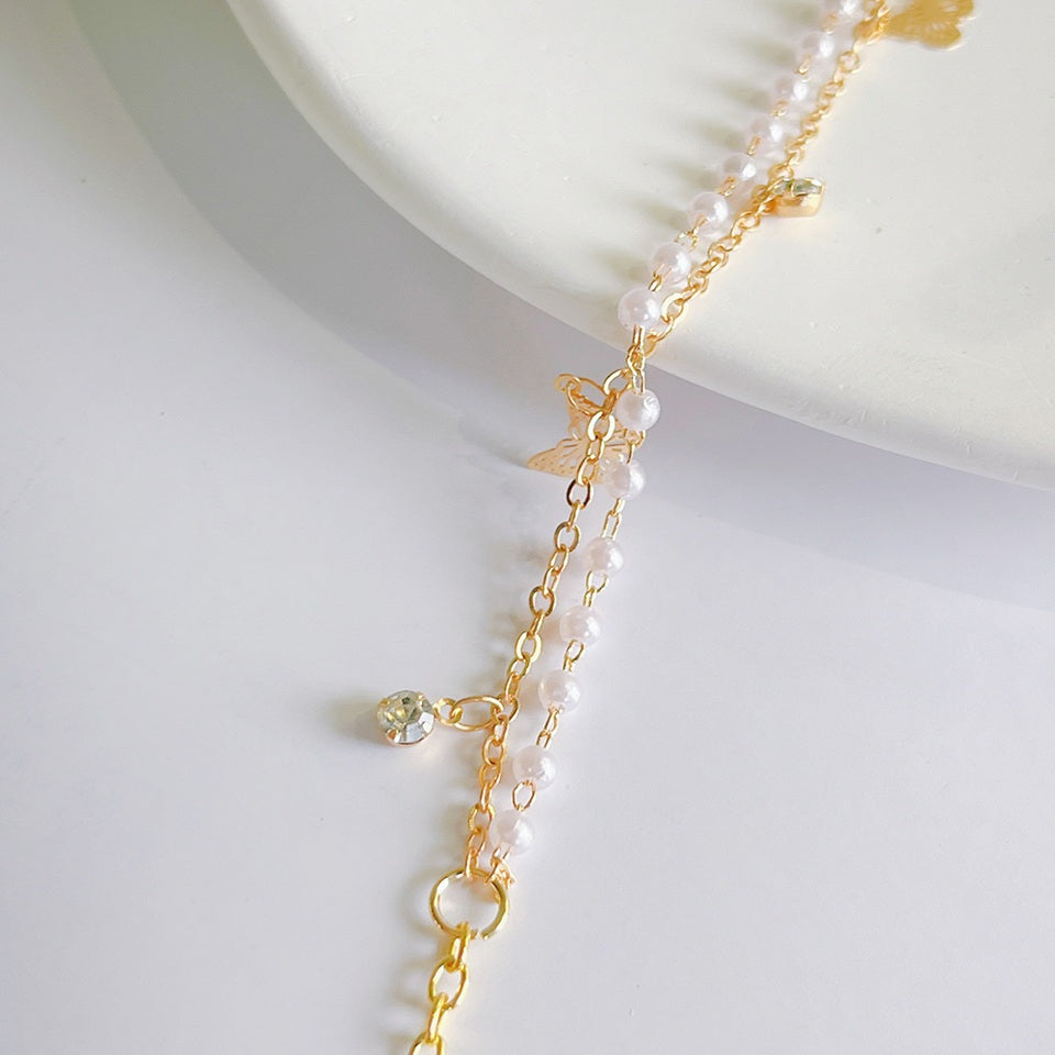 un superbe bracelet doré composé de deux chaines complémentaires. La première est faite de perles blanches et la deuxième est orné de papillons doré et de strass scintillants. L'ensemble est chic et bohème.