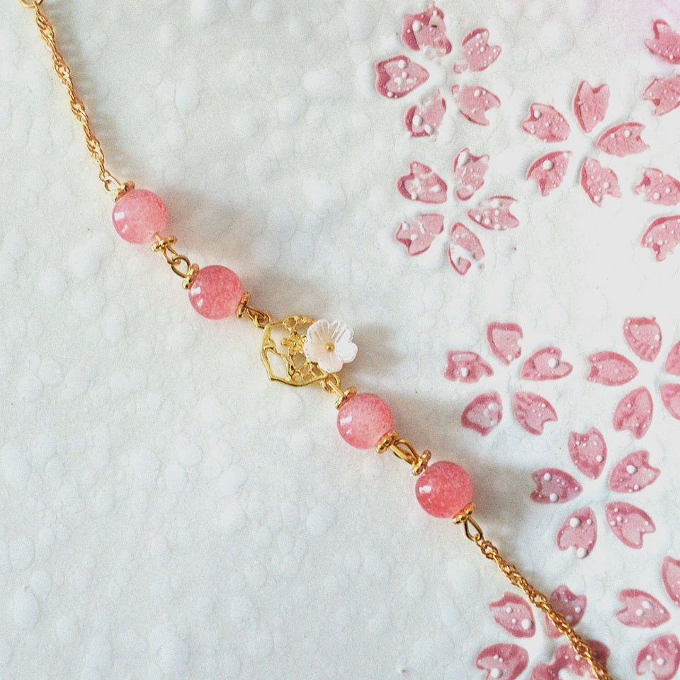 un superbe bracelet dorée de perles roses et d'une breloque fleur de sakura. L'ensemble est poétique, romantique.