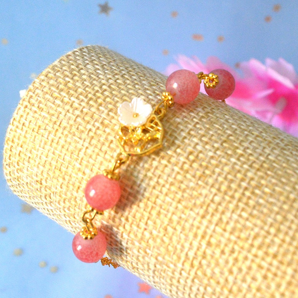 un superbe bracelet dorée de perles roses et d'une breloque fleur de sakura. L'ensemble est poétique, romantique.