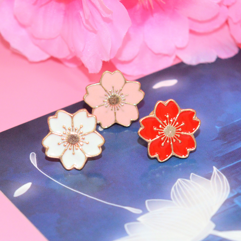 des pin's en forme de fleur de sakura colorée : noir, rouge, bleu, blanc et rose. Avec leur finition dorée, ils sont symbole de renouveau et de beauté.